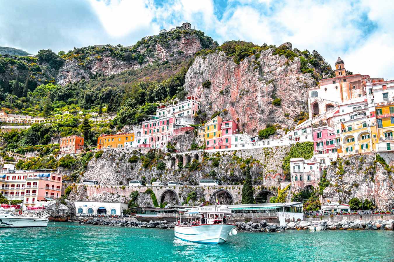 White boat docked at the Amalfi Coast port with green cliffs in the background, Italy