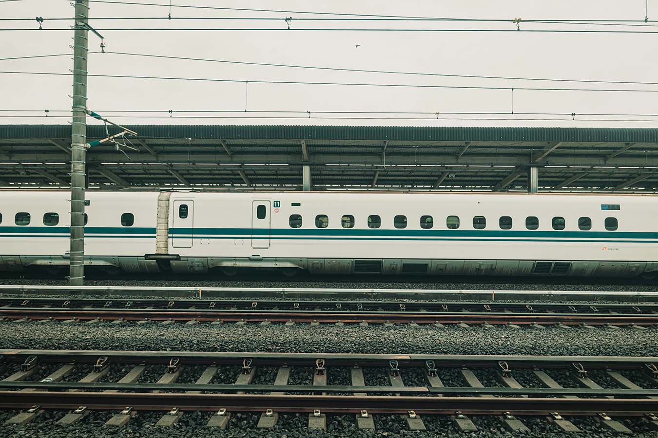A white Japanese Shinkansen bullet train stopped at a station platform with overhead wires