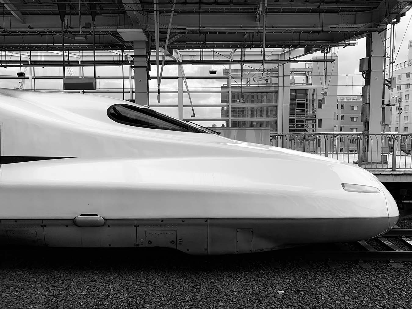 A white Shinkansen bullet train passing through Kyoto station during the day