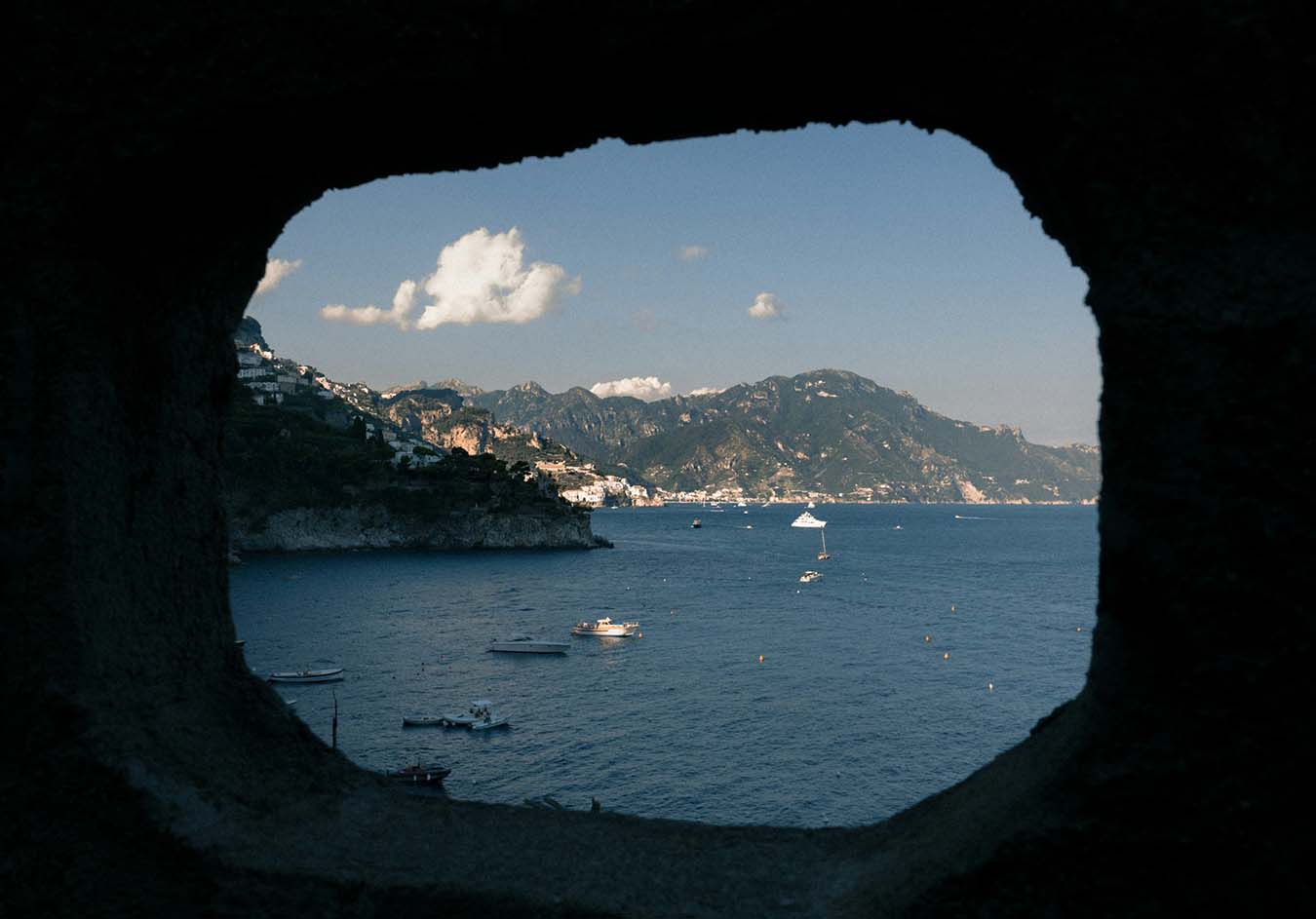 View through a rock arch to the Amalfi Coast sea with boats and cliffs, Italy